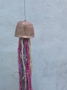 a pink and purple hat hanging from a hook on a white wall with long hair