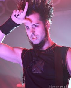 a man with spiked hair holding his hand up in the air while standing on stage