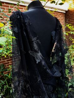 the back of a black dress with butterflies on it, in front of some bushes