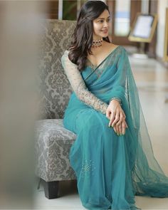 a woman in a blue sari sitting on a chair with her hand on her hip