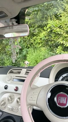 the interior of a car with pink steering wheel covers and dashboard controls, along with trees in the background