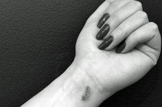 a black and white photo of a woman's arm with a small feather tattoo on it