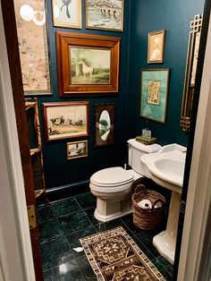 a bathroom with blue walls and pictures on the wall above the toilet, rug in front of the sink