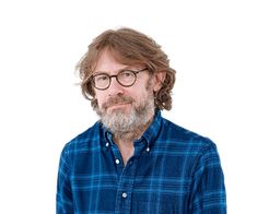 a man with glasses and a beard wearing a blue shirt is standing in front of a gray background