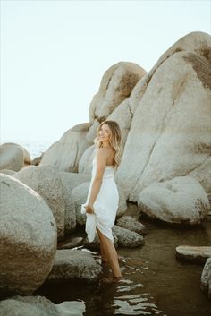 a woman standing in the water near some rocks