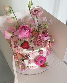 a white cake with pink flowers and strawberries on top is in a cardboard box