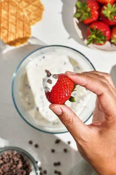 a person holding a strawberry in front of a bowl of strawberries and crackers