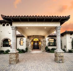 the front entrance to a large home with stone pillars and arched doorways at sunset