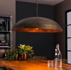 a wooden table topped with vases and bottles under a large metal light hanging from the ceiling