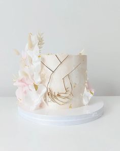 a white cake decorated with flowers and gold leaf accents on a plate against a plain background