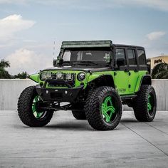 the green jeep is parked in front of a concrete wall and has bright green rims