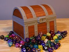 a wooden chest filled with colorful dice on top of a wooden table next to a pile of metal and wood dice