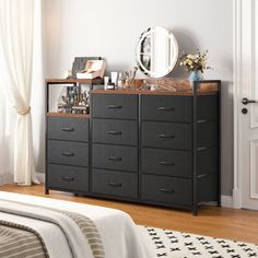 a bedroom with a bed, dresser and mirror on it's side table in front of a window