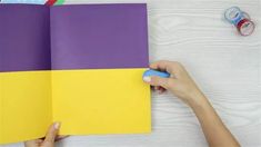 a person holding an open book on top of a wooden table next to scissors and tape