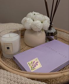 a wicker tray with a candle, book and flowers on it