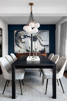 a dining room table with white chairs and a large painting on the wall behind it