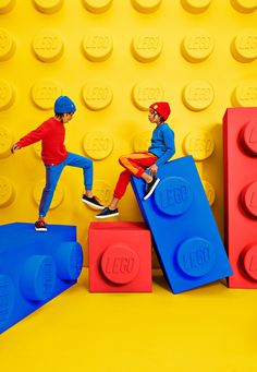 two children sitting on lego blocks in front of a yellow and blue wall with red letters