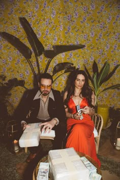 a man and woman sitting next to each other in front of a wall covered with flowers