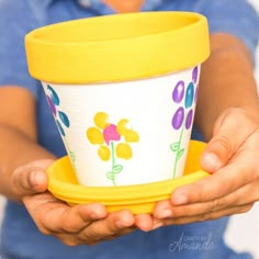 a person holding a yellow and white cup with flowers painted on the side, while wearing a blue shirt