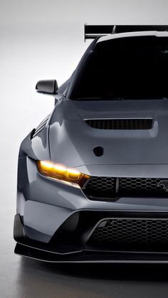 the front end of a grey sports car with its lights on and hood up, is shown