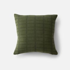 a green pillow with black squares on the front and back, sitting against a white wall