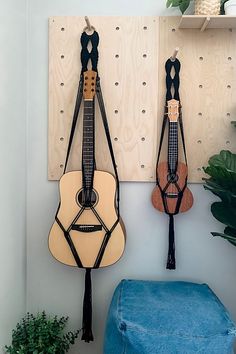 two guitars are hanging on the wall next to a blue stool and potted plant