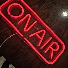 a red neon sign that says on air sitting on top of a wooden table next to a phone