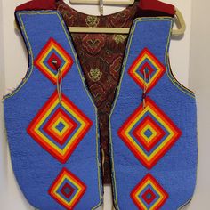 a blue vest with red, yellow and orange designs hanging on a white hanger