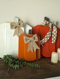 three pumpkins are sitting on a mantle with candles next to them and one has a bow