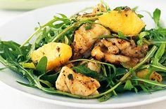 a white plate topped with chicken and green leafy salad on top of a table