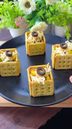 four crackers with cheese and olives on them are sitting on a black plate