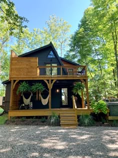 a small cabin in the woods with lots of trees and plants on the front porch