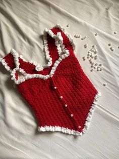 a crocheted red and white dress laying on top of a bed next to beads