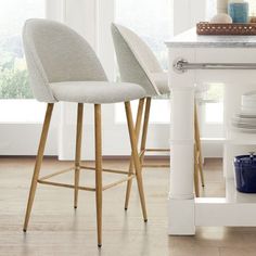 two grey bar stools sitting on top of a white counter next to a window