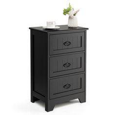 a small black cabinet with three drawers and a white vase on top of it, against a white background