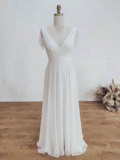 a white wedding dress on a mannequin in front of a wall with dried flowers