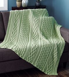 a green knitted blanket sitting on top of a couch next to a vase with flowers