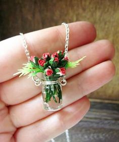 a hand holding a tiny glass jar with flowers in it on a chain that is attached to a necklace