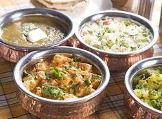 four metal bowls filled with food on top of a checkered tablecloth covered table