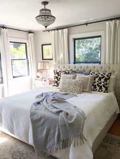 a white bed sitting in a bedroom next to two windows and a rug on the floor