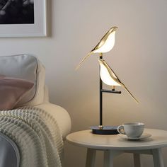 a table lamp that is on top of a white table next to a cup and saucer