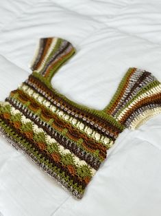 a crocheted sweater laying on top of a white bed covered in blankets and pillows