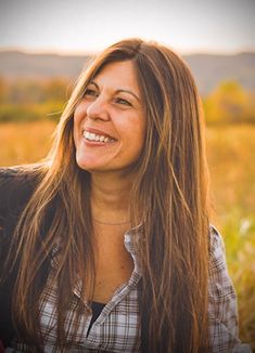 a woman sitting in a field smiling at the camera