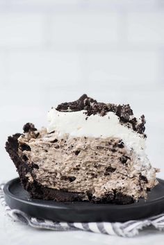 a piece of cake on a black plate with white frosting and oreo cookies