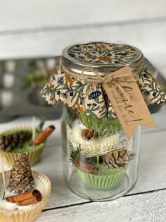 some cupcakes are in the glass jar with pine cones and other things inside