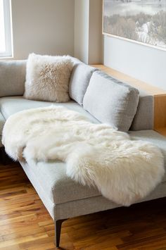 a couch with white fur on it in front of a window and wood flooring