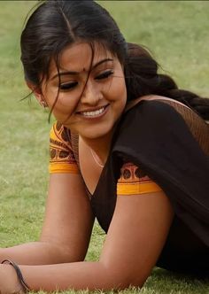 a woman laying on the grass with her hand in her pocket and smiling at the camera