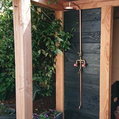 an outdoor shower in the middle of a wooden structure with plants growing on it's sides