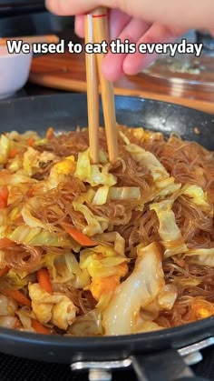 a wok filled with noodles and vegetables being stir fried by chopsticks in it