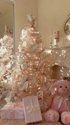 a pink teddy bear sitting in front of a white christmas tree with presents under it